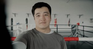 Portrait of joyful Asian sportsman making online video call from gym talking and showing uniform looking at camera. Sports and communication concept.