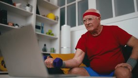 Funny senior man lifting dumbbells while watching online tutorial, fitness buff