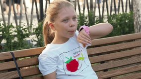 Little girl in the park talking on a smart watch.Children's electronic watch on a child's hand is an alternative to a smartphone. Press on the digital clock display.Modern parental control for a child
