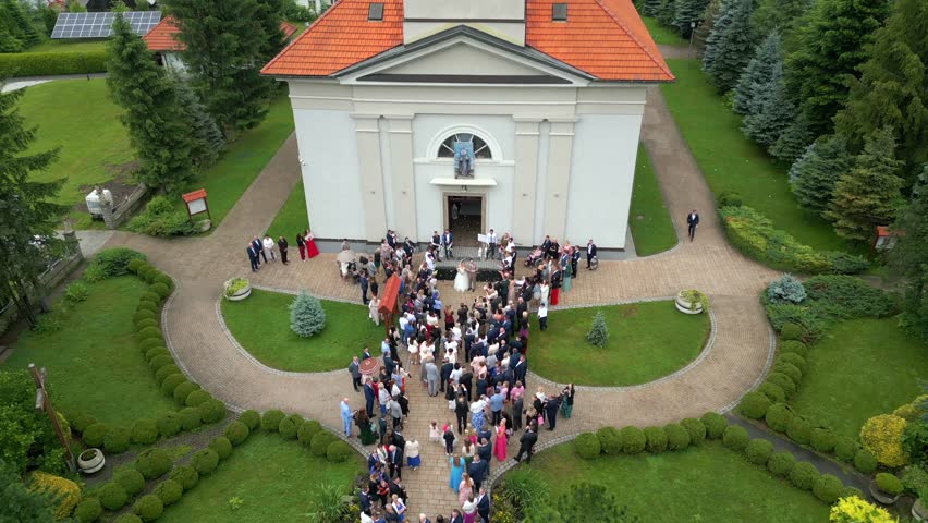 Aerial view of the bride and groom with family and guests gathered in front of the church after the wedding ceremony.