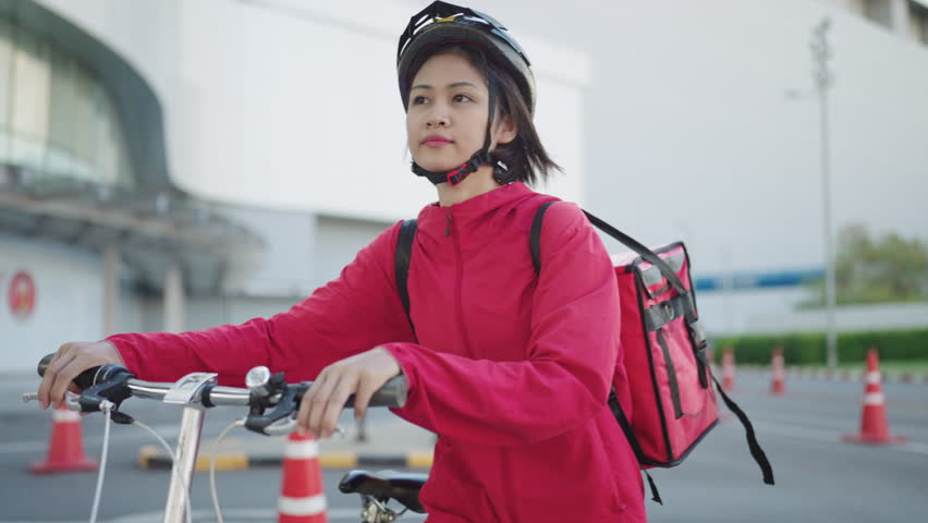 delivery Asian woman with red backpack rides a bicycle through the city with food delivery,Food delivery concept