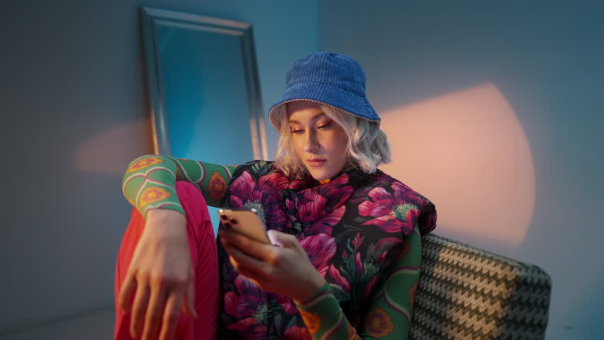 Beautiful young stylish woman sitting and searching internet and social media on her smartphone