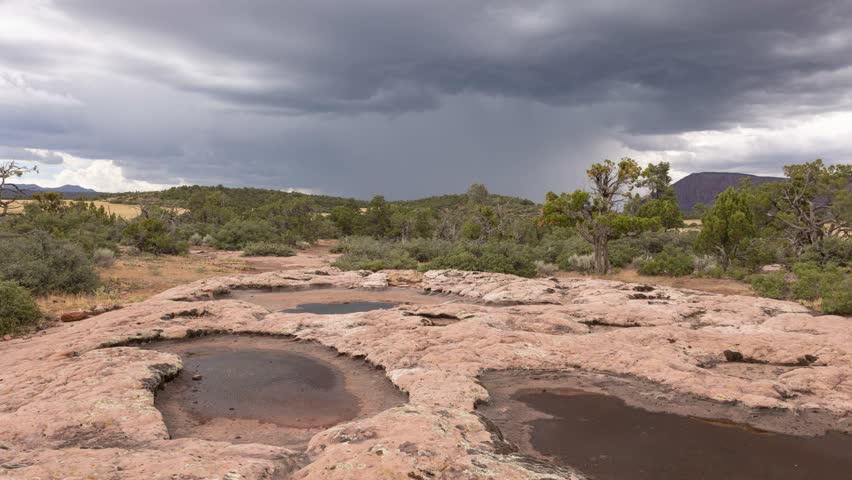 A 4K time lapse video of a summer monsoon storm on the horizon seen from a rocky ridge with some ephemeral pools that are beginning to dry up. A couple of lightning bolts strike the distant mountain. Royalty-Free Stock Footage #1107464497