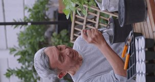 Vertical clip. Happy retired man spending time planting plants at home. An elderly Asian man gardening at home.