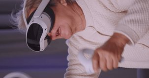 Vertical clip. Asian old woman having fun playing games while wearing virtual reality glasses at home.