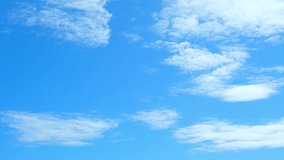 The sky time-lapse is a brilliant expanse of cerulean blue, stretching infinitely in all directions. Wisps of cotton-white clouds drift lazily across the screen. Timelapse. sky background.
