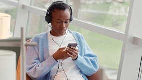African Black teenage girl university or college student refugee sitting in chair in university campus, coworking office space or airport lounge, wearing headphones looking away at window. - Powered by Shutterstock - Get 15% off with code: PIKWIZARD15