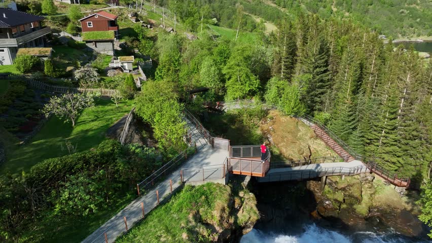 One man standing on Geiranger river viewpoint above waterfall - Aerial view unweiling Geiranger fjord in background