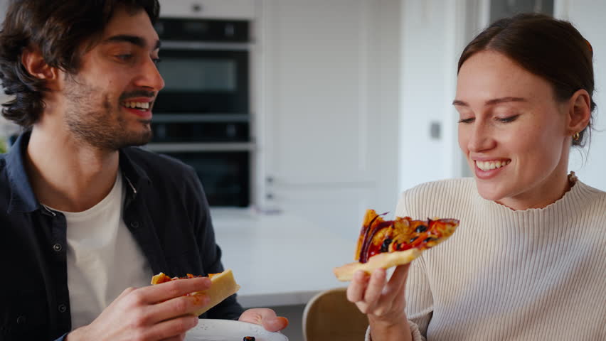 Close up of couple in kitchen at home eating fresh homemade pizza from the oven - shot in slow motion