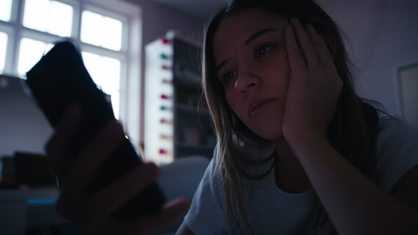 Depressed teenage girl lying on bed at home looking at bullying messages on mobile phone - shot in slow motion Royalty-Free Stock Footage #1107476621