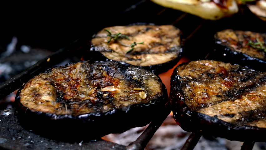 Grilled eggplant rings preparing on barbecue grill on charcoal and flame tongue. Fried aubergines as vegetarian and vegan healthy Mediterranean food. Close up. Royalty-Free Stock Footage #1107479469