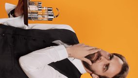 Vertical video Skilled butler calculating meal prices to give check to clients on camera, serving customers with food or drinks against yellow background. Elegant employee in suit acting thoughtful in - Powered by Shutterstock - Get 15% off with code: PIKWIZARD15