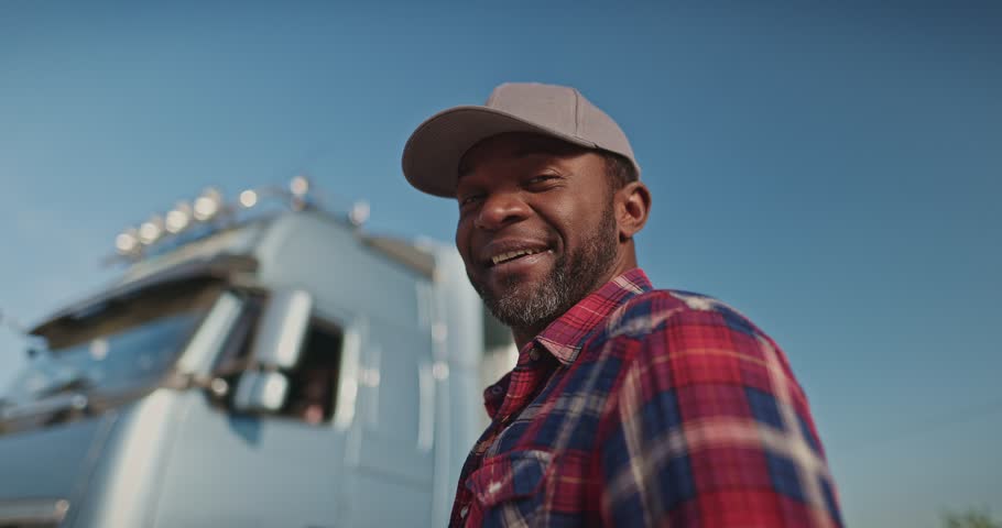 Bottom view of satisfied African American owner of lory. Driver looking with optimism at camera and afterwards at his truck. Fixing hat while being proud of new purchase. Smiling from delivery. Royalty-Free Stock Footage #1107486805