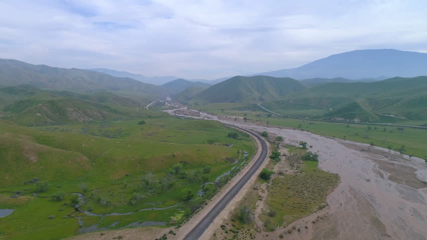 Aerial Shot Of Freight Train On Track Near River And Plants, Drone Flying Forward Over Landscape Against Cloudy Sky - Bakersfield, California
