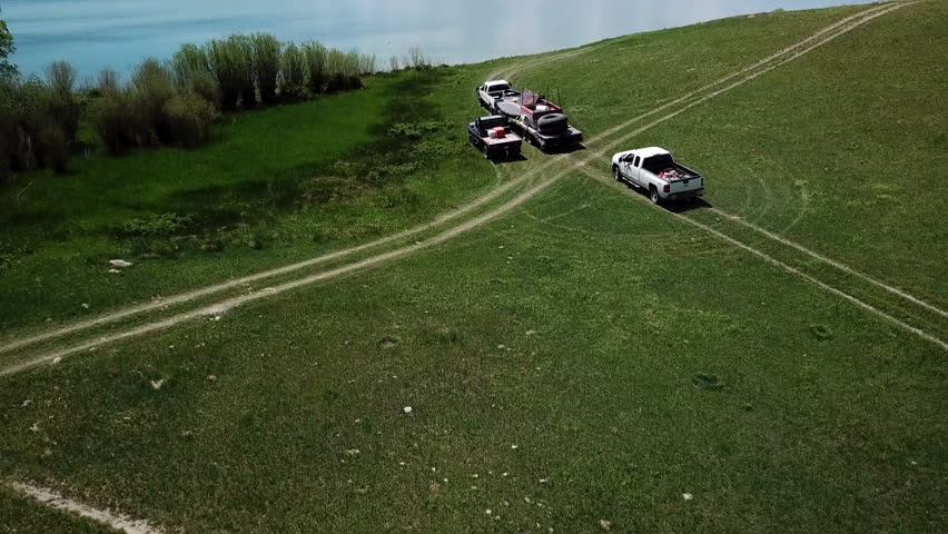 Aerial Panning Shot Of Vehicles And Dogs On Green Hill Near Lake During Sunny Day - Billings, Montana