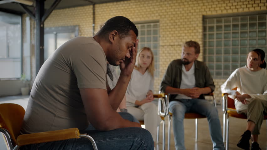 Side view of african american man being wrapped up in his thoughts while multiracial group members having discussion. Anxious individual struggling with detrimental fear of social interactions. | Shutterstock HD Video #1107494187