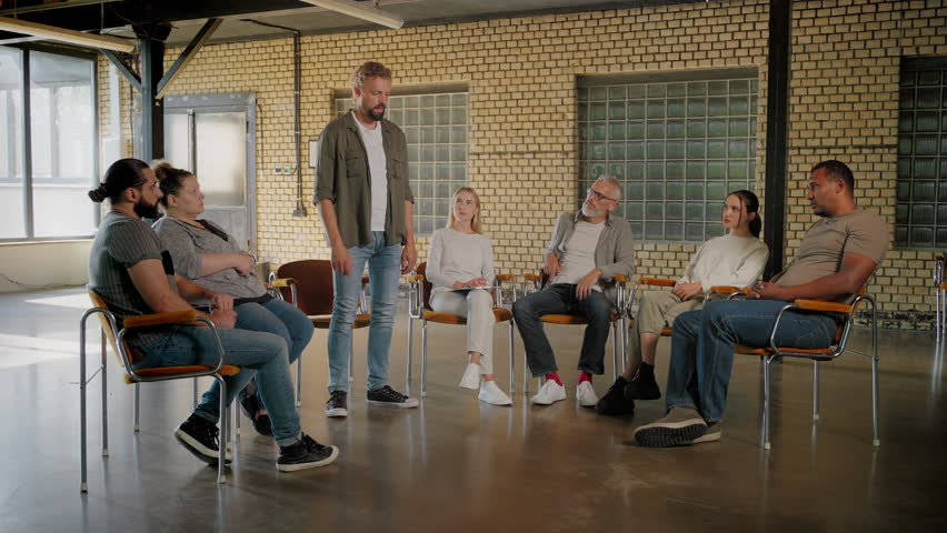Middle-aged bearded man talking with hand on heart while being followed by applause from group therapy members. Caucasian adult struggling with addiction describing accomplishments since last meeting.