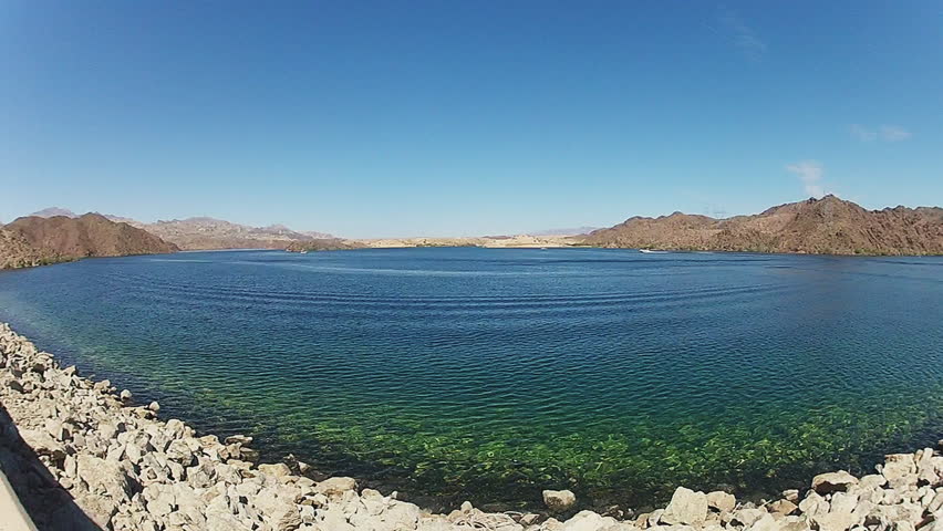 Super wide angle shot of Lake Mohave behind Davis Dam on the Colorado River in Laughlin Nevada. Gentle ripples of cool green blue clear water lap at the rocky edge of the desert dam.