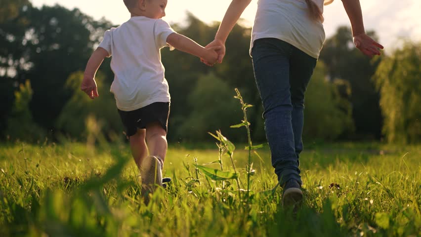 children run in the park. boy and a girl holding hands run through the grass in the summer at sunset in the park. happy family kid dream concept. children run at sunset in summer hold hands sun