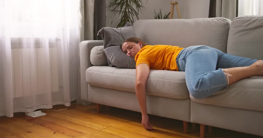 Tired woman sleeping on sofa at home while robot vacuum cleaner working on floor