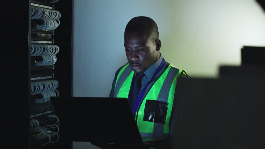 Man, electrician and computer in server room inspection, cybersecurity maintenance and cables or hardware solution. Technician or african person engineering on laptop, electricity and power at night - Powered by Shutterstock - Get 15% off with code: PIKWIZARD15