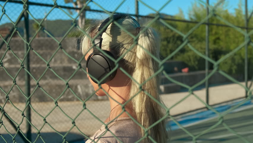 Listening music while relaxing on ground. A smiling teen girl listen tunes by the mesh and pass her weekend on sport ground.