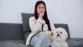 Beautiful young asian woman and dog sitting on sofa watching movie on television for leisure in living room at home, girl and pet on couch looking cinema on tv, lifestyles and entertainment concept.