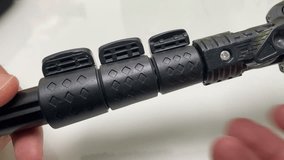 Hand adjusting locking screw handle to loosen and lock black metal tripod leg on white background