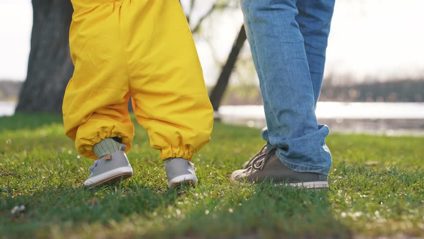 baby toddler takes first steps in nature. happy family a child dream concept. baby steps on the green grass in nature first steps close-up. family dad teaches baby son on lifestyle the park