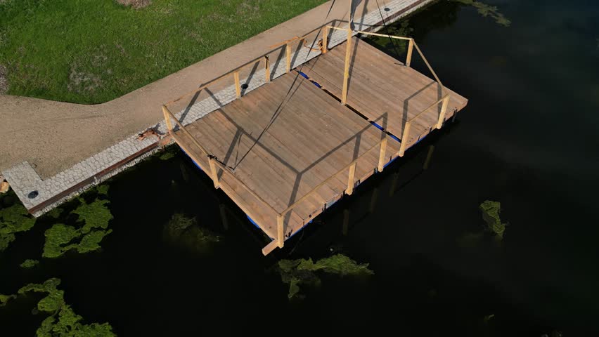 Pier for park visitors. two steps lead to it. planks terrace over water. Pond with a dock for boats. floor plan of a rectangle. the terrace has no railings., stone, green, algae, boat, lawn