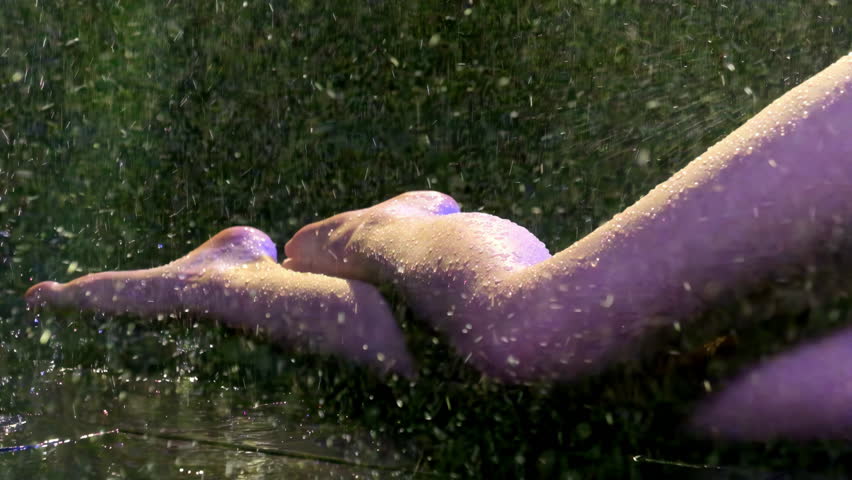 Skinny woman sits in puddle on the floor. Under strong stream of water, slender legs of young woman wet and cover with drops.