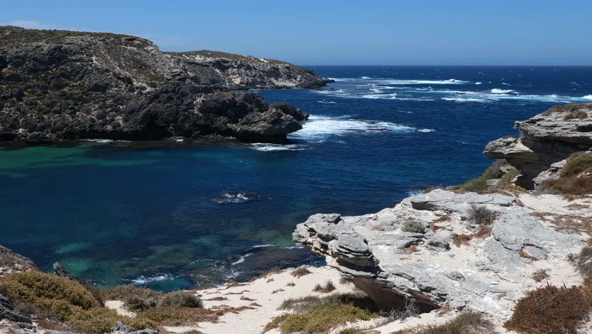 Water splashing on the cliffs of Rottnest Island, Western Australia. Beautiful wild and rocky landscape of Rottnest Island. Dark blue sea around rocky cliffs. Sunny day on Australian island.