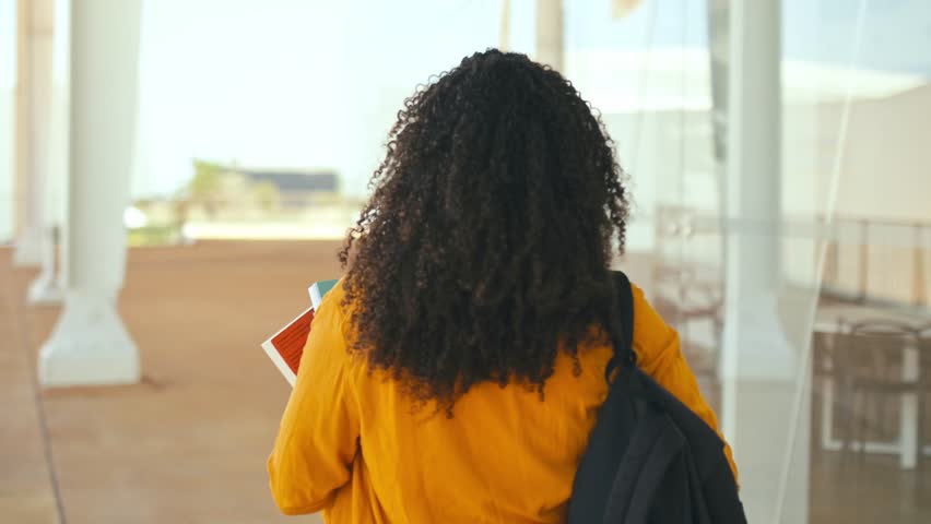 Positive trendy female student. Happy lovely brazilian or hispanic female student, with a backpack and notebooks in her hand, walks near the university campus, turns and smiles at the camera Royalty-Free Stock Footage #1107538871