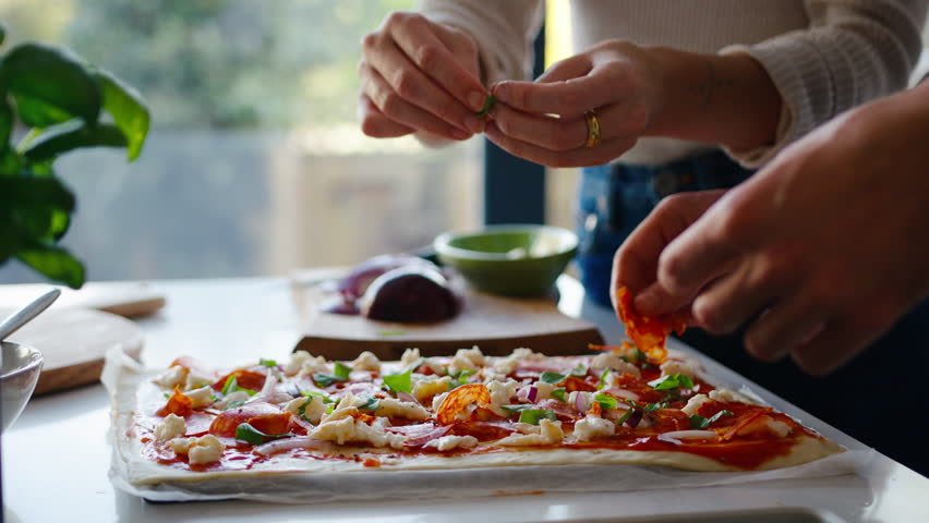 Close up of couple in kitchen at home making fresh pizza and putting it into the oven - shot in slow motion