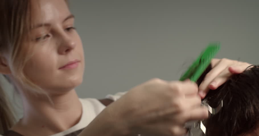 Soft focus Hairdresser wets the hair with a spray and combs it. Stylish man is sitting in the barbershop. Hairdresser Woman cutting hair. Attractive man getting his hair cut in a modern barbershop. 4K