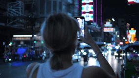 Attractive Young Tourist Woman Holding Smartphone and Recording Video of Busy Night Chinatown Street Traffic. High Quality 4K Slowmotion Cinematic Lifestyle Travel Concept Footage. Bangkok, Thailand.