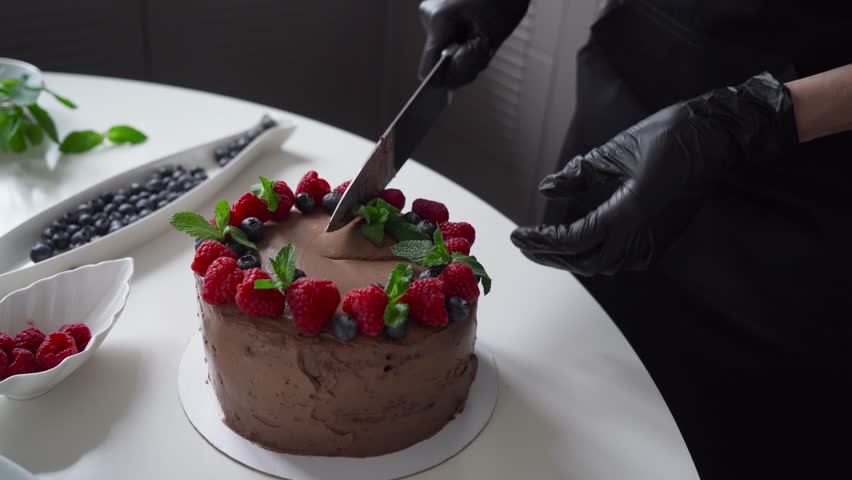 Pastry chef cuts chocolate cake with berries.