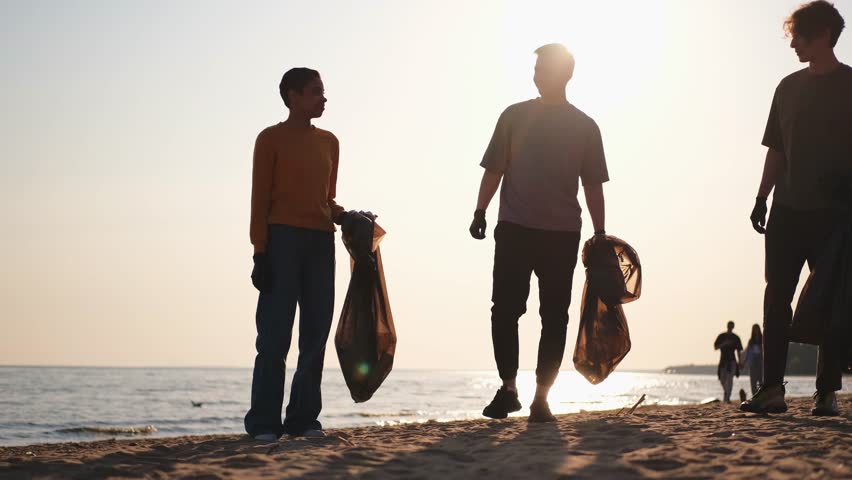 Earth day. Volunteers activists collects garbage cleaning of beach coastal zone. Woman mans with trash in garbage bag give high five on ocean shore. Environmental conservation coastal zone cleaning Royalty-Free Stock Footage #1107549371