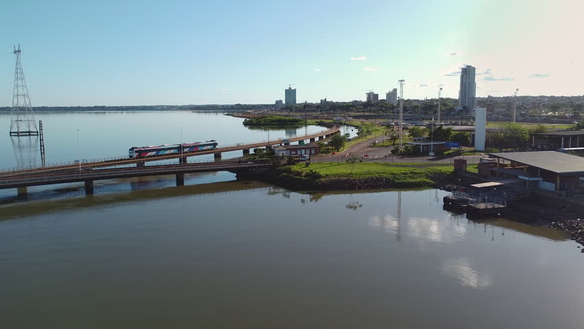 A cityscape containing a train crossing over the Rio Parana River, Puente Internacional Posadas - Encarnación and cars driving on the bridge. The bridge is located in Posadas, Misiones, Argentina. 