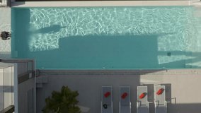 Top view video of outdoor pool with sun loungers on side, man in black shorts dives and swims from one end to the other, summer lifestyle concept