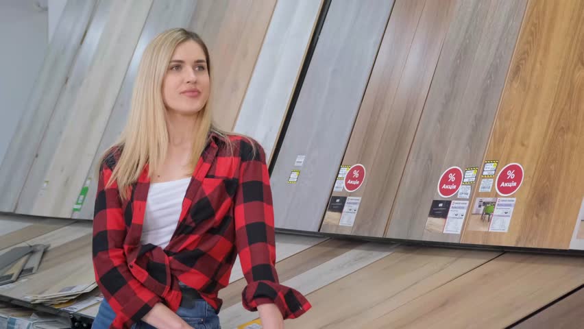 A beautiful blonde woman sits in a construction supermarket on a wooden floor background. 