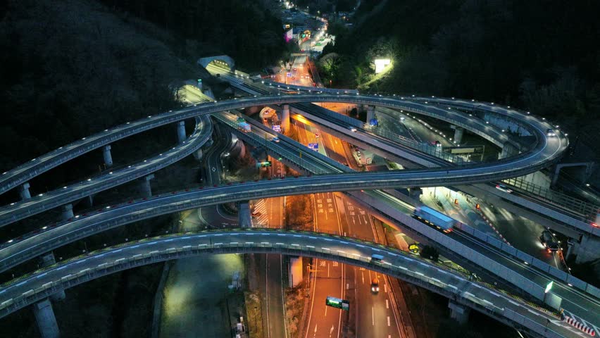 drone shot of traffic on highway intersection and convergence of roads in city at night, urban transportation and infrastructure, traffic regulations are written in Japanese on the road