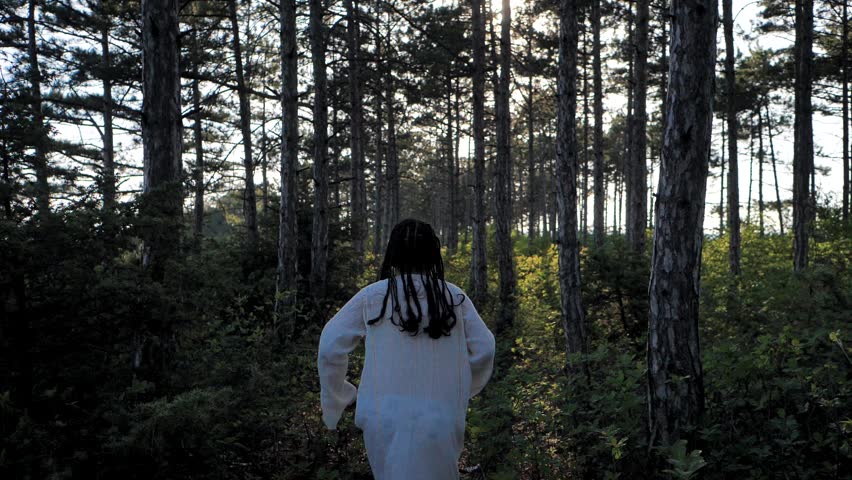 A little girl with afro pigtails runs in a white dress through the woods