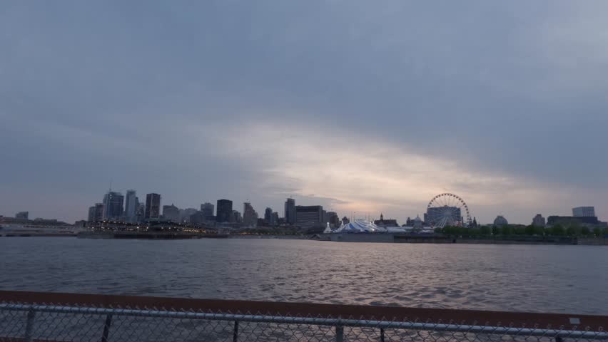 Sunset to Night Time Lapse of the Downtown Montreal Skyline From Across the Water, With Beautiful Sky, City Lights, and a Fence in the Foreground