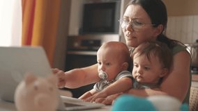 mother works remotely from home with two babies in her arms. pandemic remote work concept. mom tries to work at home in fun kitchen, small children interfere with sitting business in her arms - Powered by Shutterstock - Get 15% off with code: PIKWIZARD15