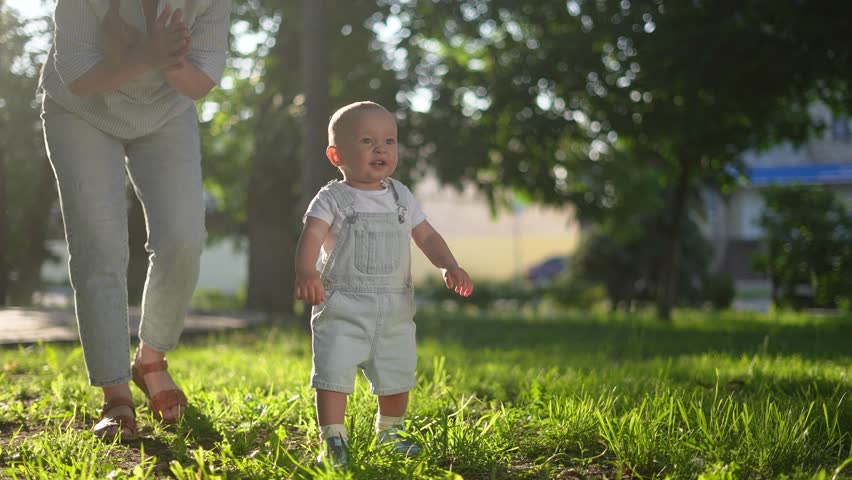 baby first steps in the park. happy family in park on vacation. mother teaches baby son to take the first steps on the green grass in the summer in the park. happy family kid concept dream