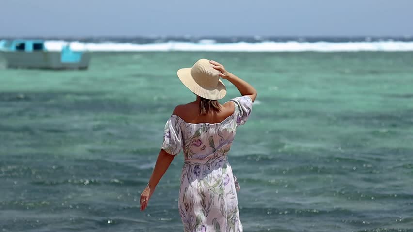 Young woman back view wearing hat and dress sea waves turquoise water boat summer vacation