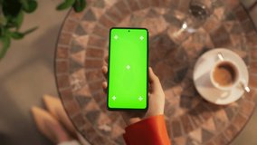 POV of a Woman Sitting at a Coffee Table, Holding a Smartphone Device, Looking at a Screen with Green Chromakey Mock Up Display. Video Template with Placeholders for Digital Marketing Campaign - Powered by Shutterstock - Get 15% off with code: PIKWIZARD15
