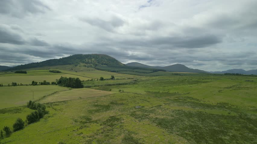 Farmland patchwork fields flying towards distant hill Great Mell Fell on cloudy summer day. English Lake District, Cumbria, UK.