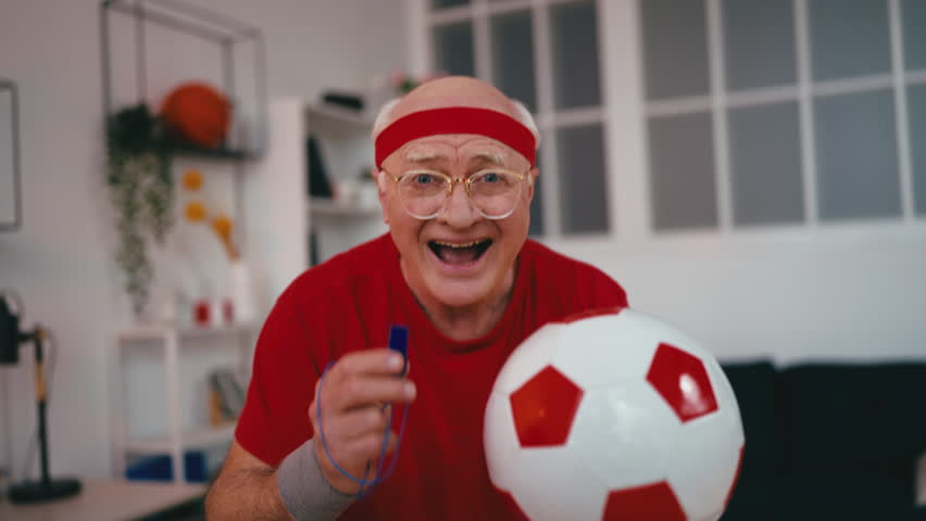 Funny senior man with whistle and ball cheering for his favorite soccer team